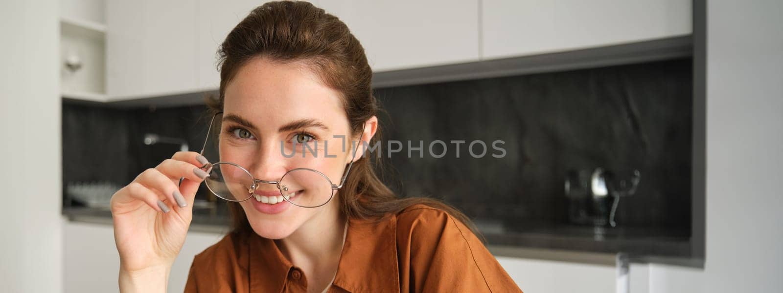 Close up portrait of carefree woman in glasses, sitting at home in kitchen, smiling and looking happy.