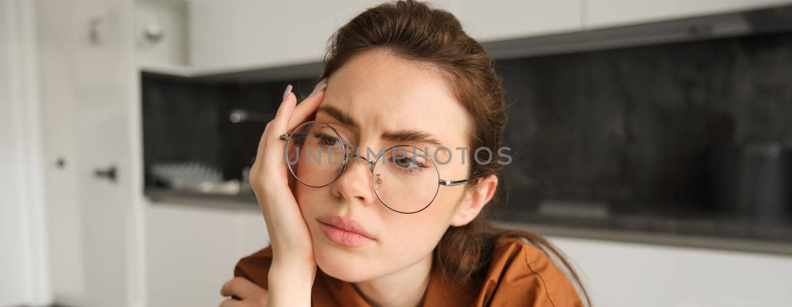 Portrait of woman thinking about something concerning, wearing glasses, touching head, sitting troubled at home.
