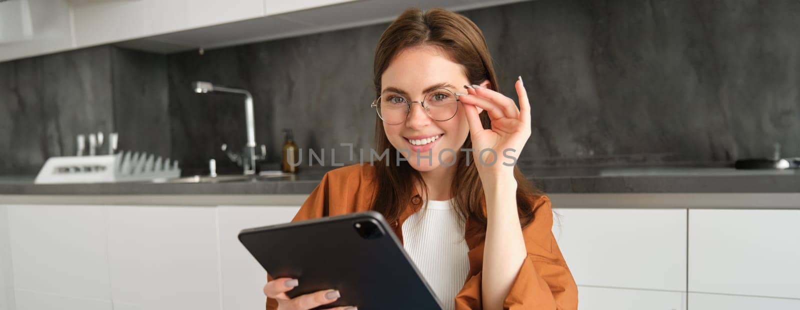 Portrait of beautiful young brunette woman, holding digital tablet, reading with glasses, smiling, surfing the net using gadget by Benzoix