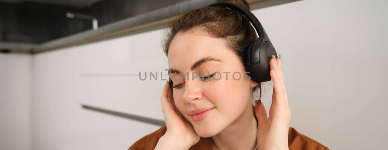 Close up shot of modern stylish woman in headphones, relaxes while listens to music in wireless earphones.