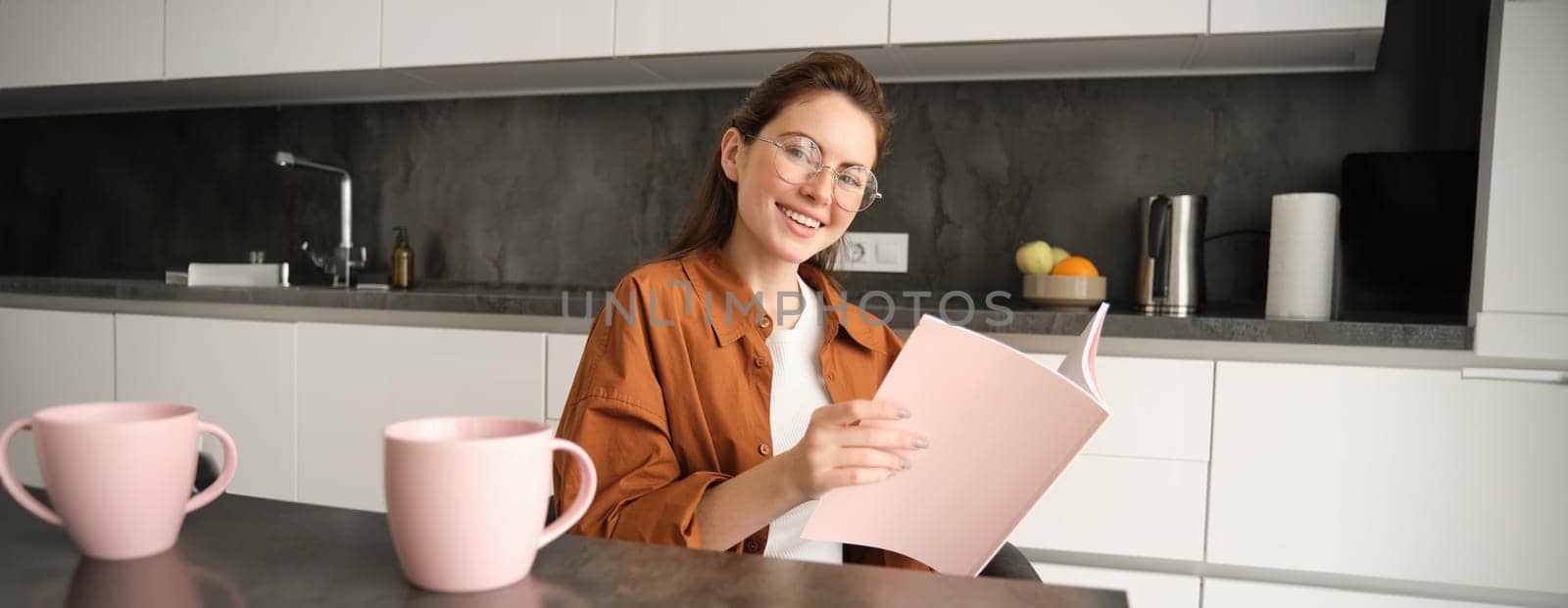 Portrait of young woman working from home, self-employed entrepreneur reading her documents, sitting at home in kitchen, wearing glasses by Benzoix