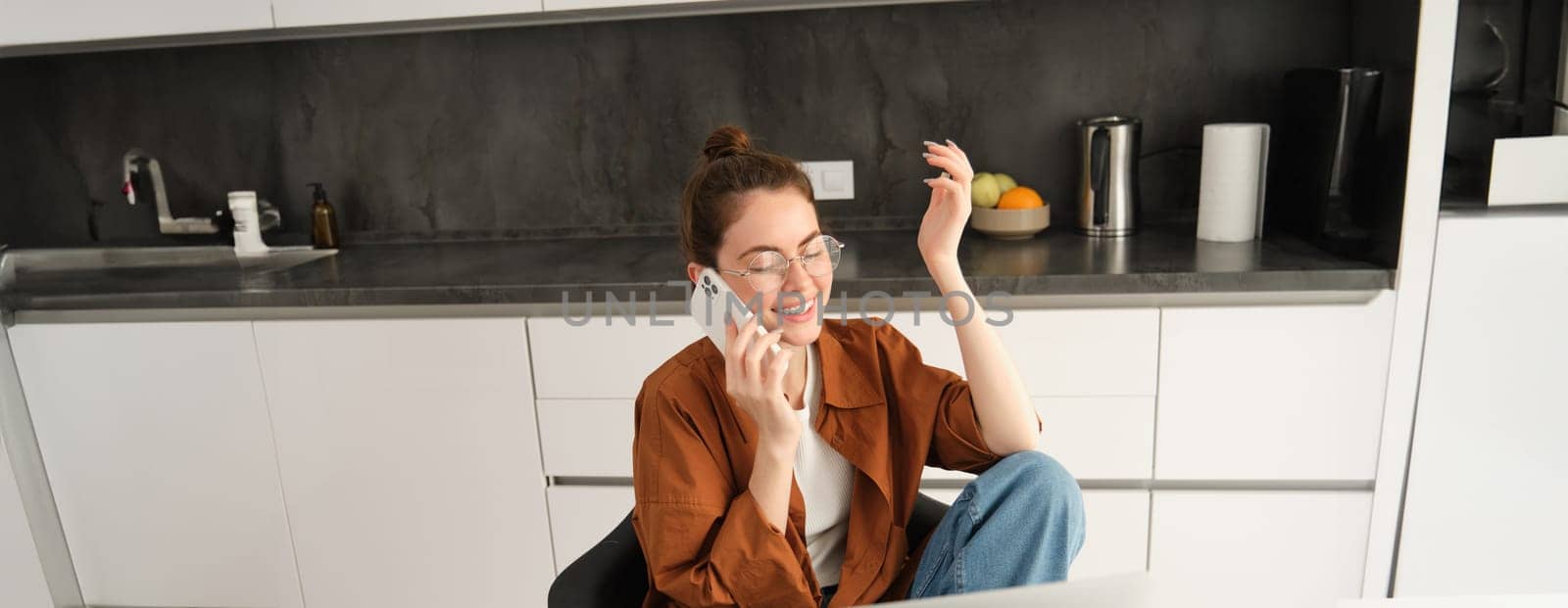 Portrait of young professional, business owner at home, talking on mobile phone, calling coworker while working on remote. Student studying and answer telephone, sitting near laptop.