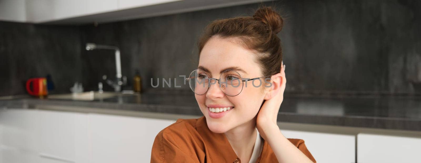 Close up portrait of brunette woman in glasses, beautiful female model sitting in kitchen, laughing and smiling, express carefree, positive emotion.