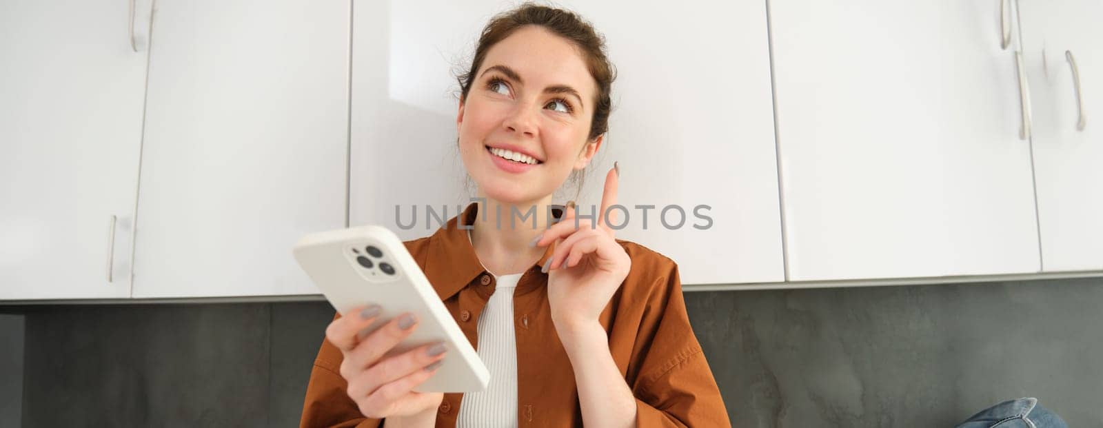 Portrait of beautiful young woman, smiling with pleased face, thinking, using smartphone application.