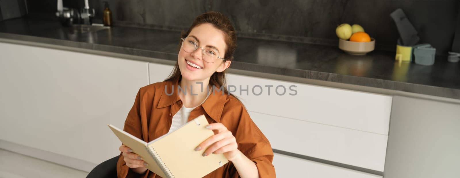 Close up portrait of beautiful young woman holding notebook, reading planner, sitting at home and studying, revising or doing homework.
