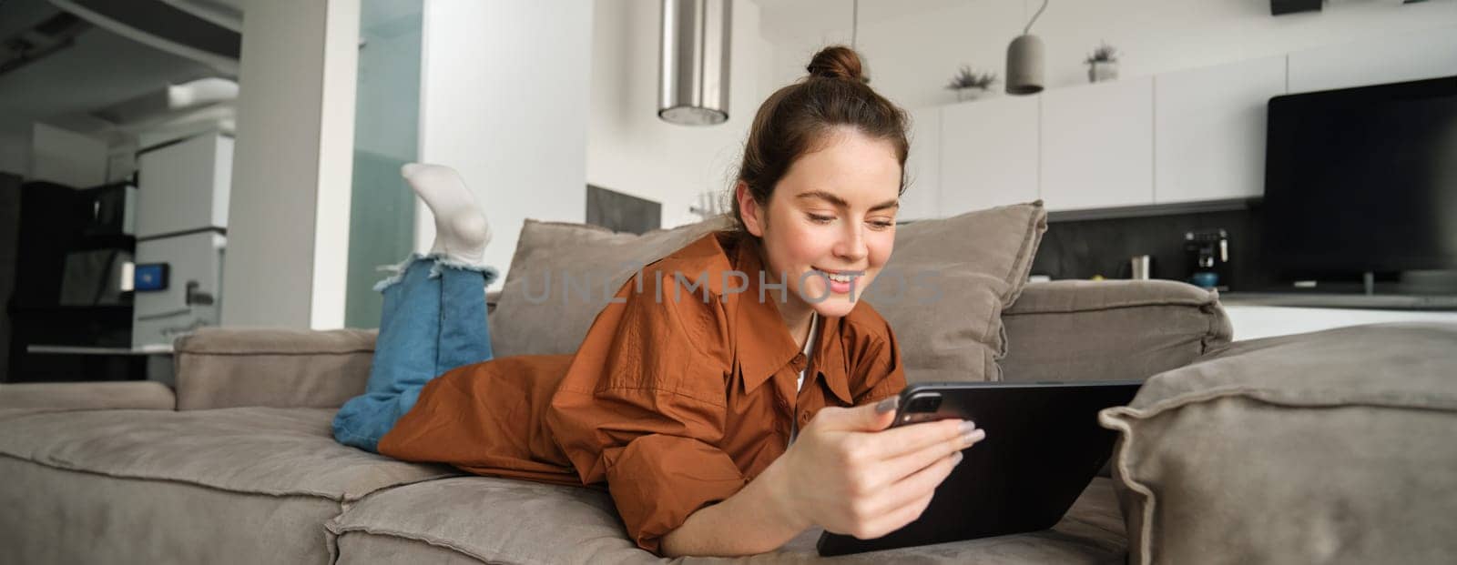 Weekend and lifestyle concept. Young woman lying on couch with digital tablet, scrolling social media, reading e-book or watching tv series on app.