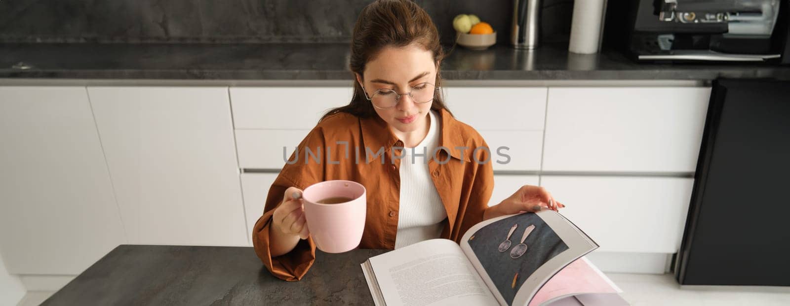 Distance learning. Young woman at home, student studying at home and drinking tea, reading her work book, revising for exam.