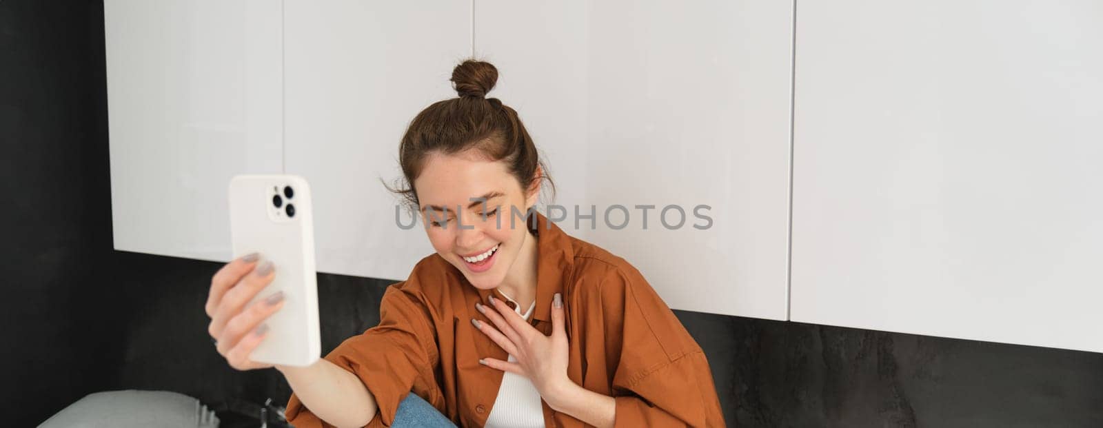 Lifestyle shot of young woman video chatting, using smartphone app to talk online, records herself for social media blog, looks happy.