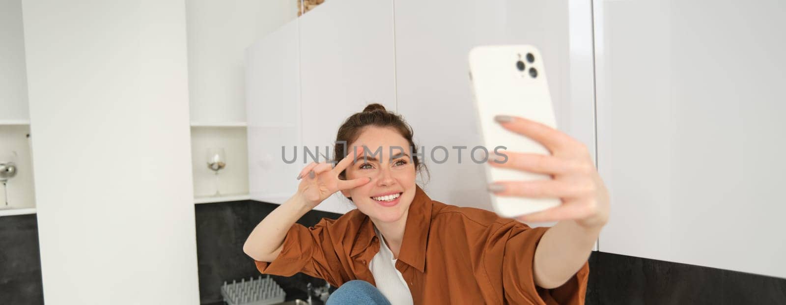 Portrait of beautiful young woman takes selfie on her smartphone, posing for photos, using filter app to take pictures for herself by Benzoix