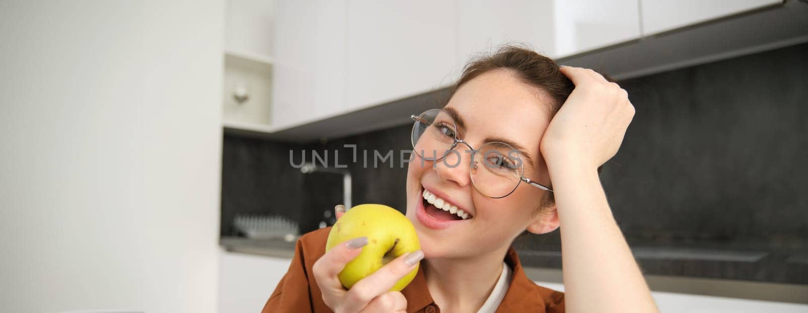 Close up portrait of happy, stylish young woman at home, biting an apple, eating fruits at home.