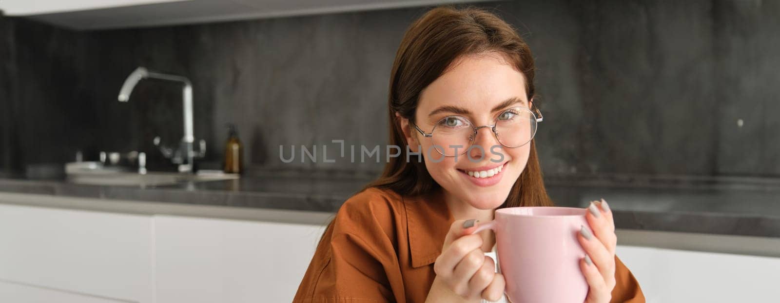 Close up portrait of cute smiling woman, spends time at home, sits in kitchen with cup of coffee, drinks tea, relaxes.