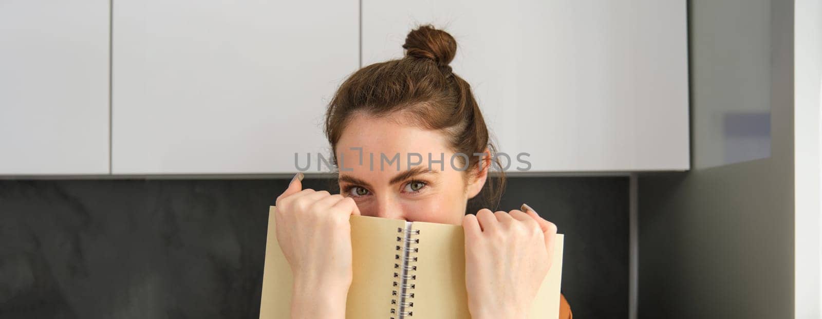 Cute romantic woman, hiding face behind notebook, smiling with eyes by Benzoix