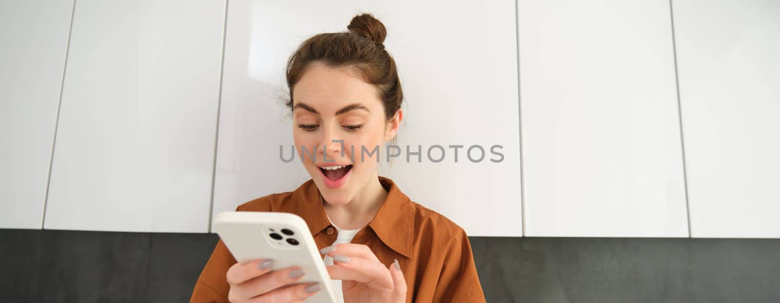 Portrait of woman looking with excitement at smartphone, found something at online shopping app, order on mobile application.