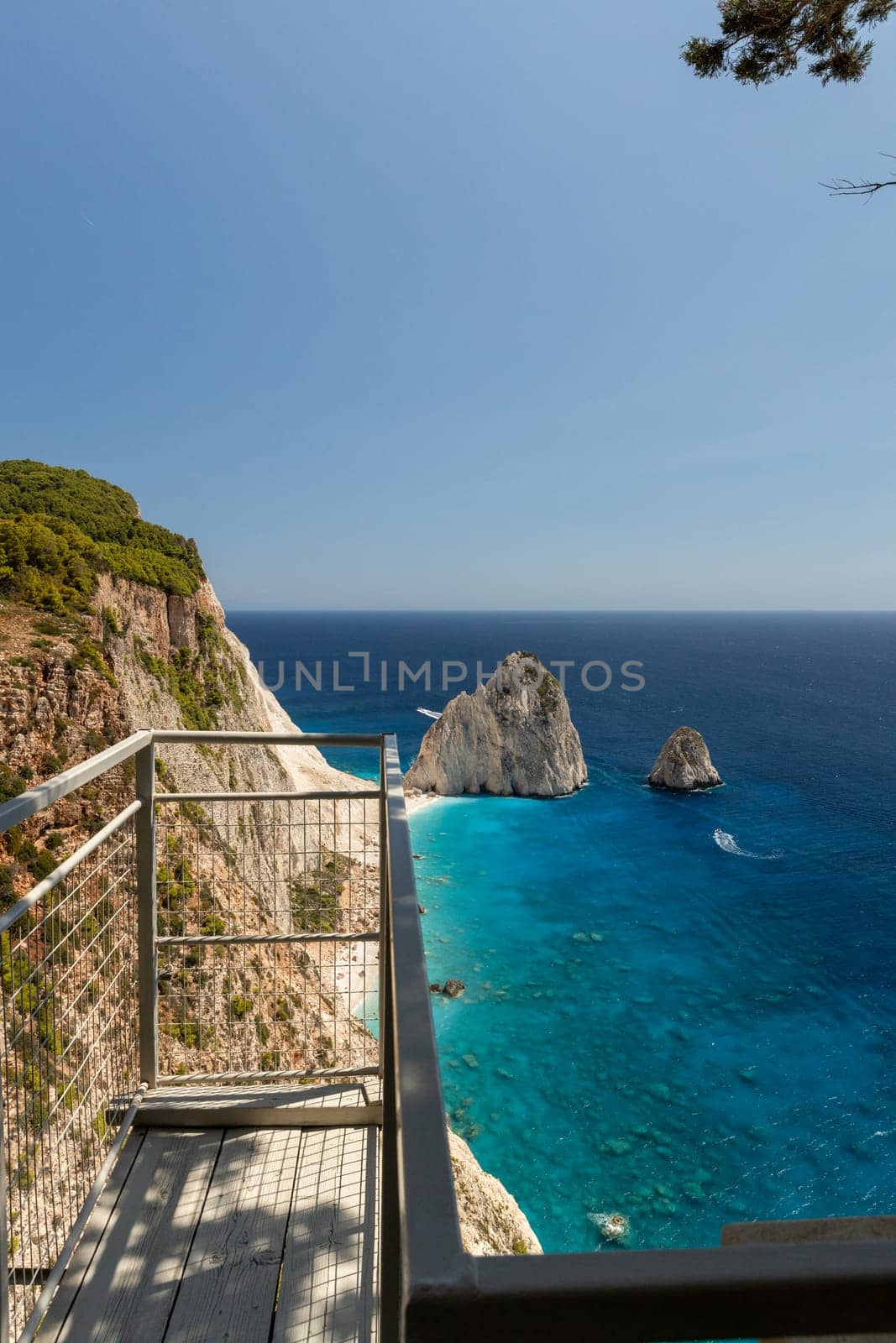Beautiful view of the observation deck and two rocks in the blue sea with passing boats near the beach coastline on a sunny summer day, close-up side view.