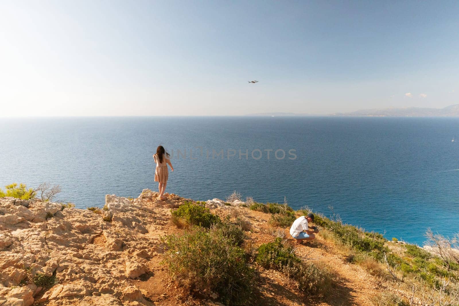 One young Caucasian couple is filming a summer video by the sea on the top of a mountain, close-up side view.