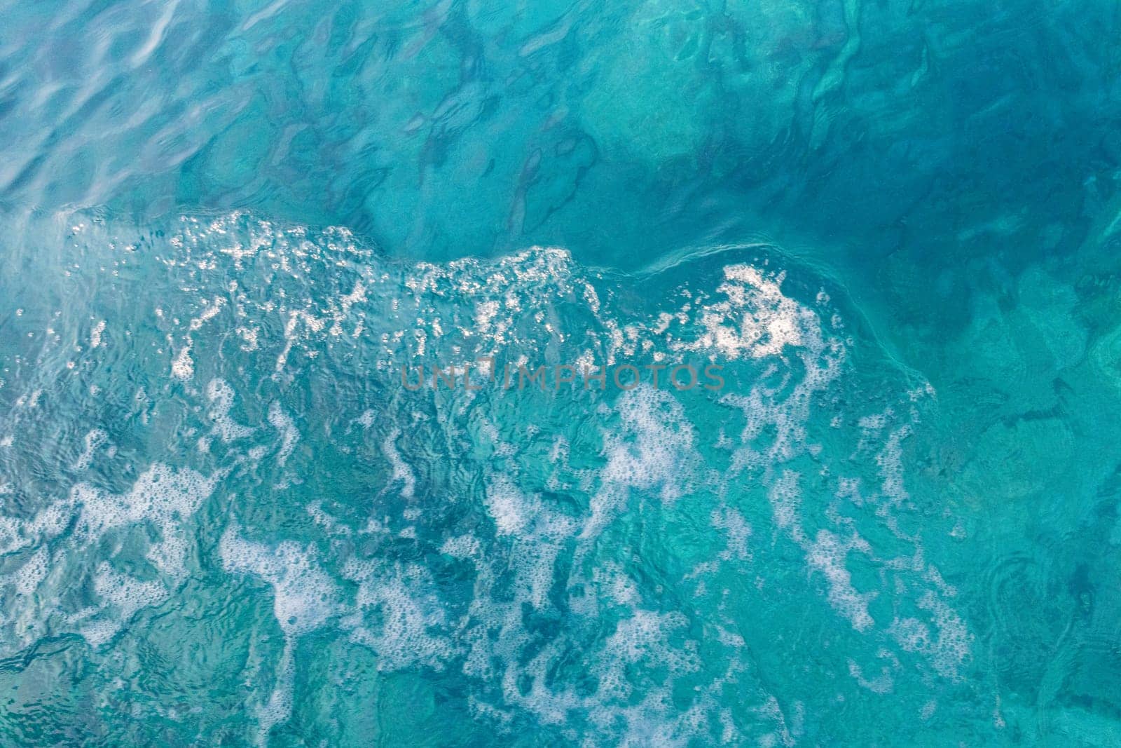 Beautiful view of blue colored water with a white foamy wave in the center on a sunny summer day, close up view from above.