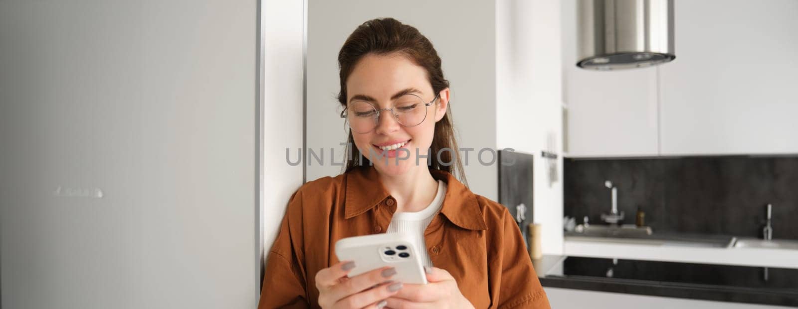 Portrait of woman at home, reading message on smartphone, checking her mobile phone app, standing with telephone by Benzoix