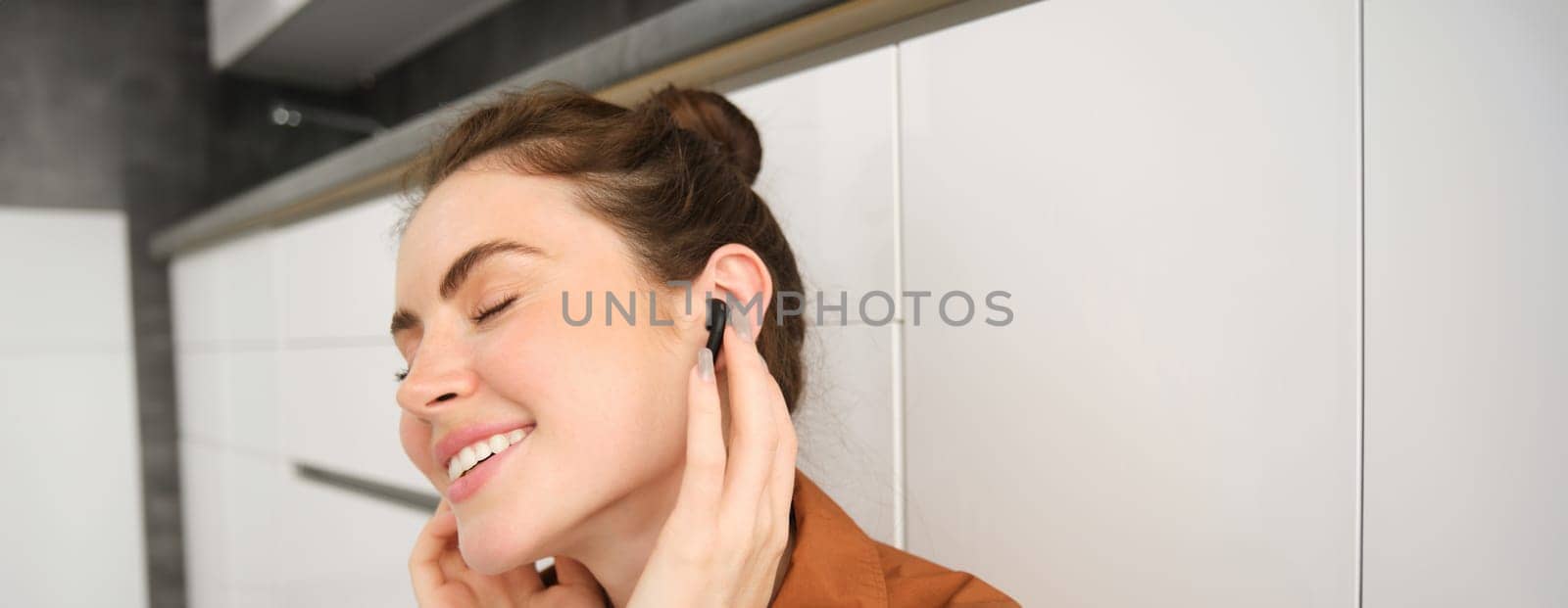 Close up portrait of woman smiling from sound quality in her wireless black earphones, listening to music in headphones, she has pleased face and eyes closed from satisfaction by Benzoix