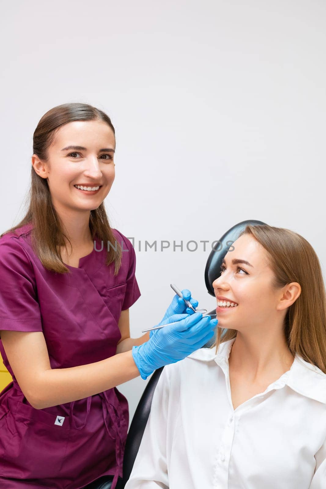 Happy young female dentist making treatment of teeth for blonde lady patient.