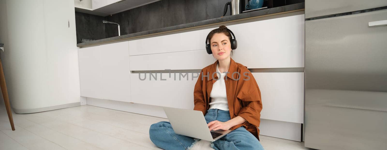 Remote workplace. Young woman works from home, sits on floor with headphones and laptop, student doing homework, studying online.