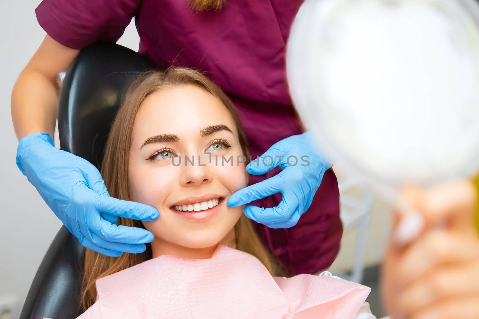 Dentist demonstrates the perfect smile of the patient after implatation of dental veneers or teeth whitening.