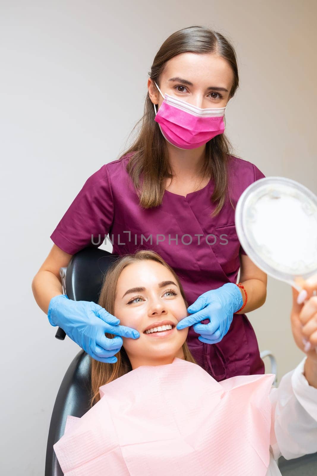 Young woman smiling while looking at mirror while doctor demonstrating the results of work by vladimka