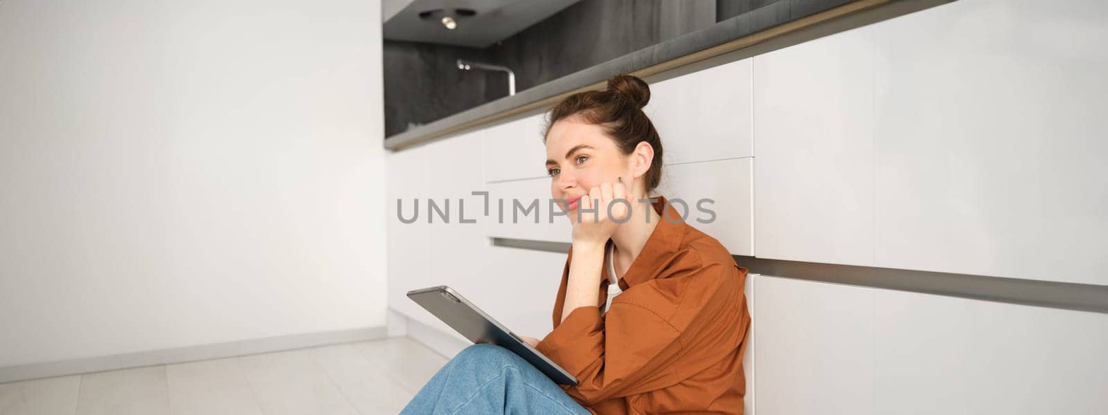 Portrait of cute young woman, freelancer working from home, sitting on kitchen floor with digital tablet and smiling by Benzoix