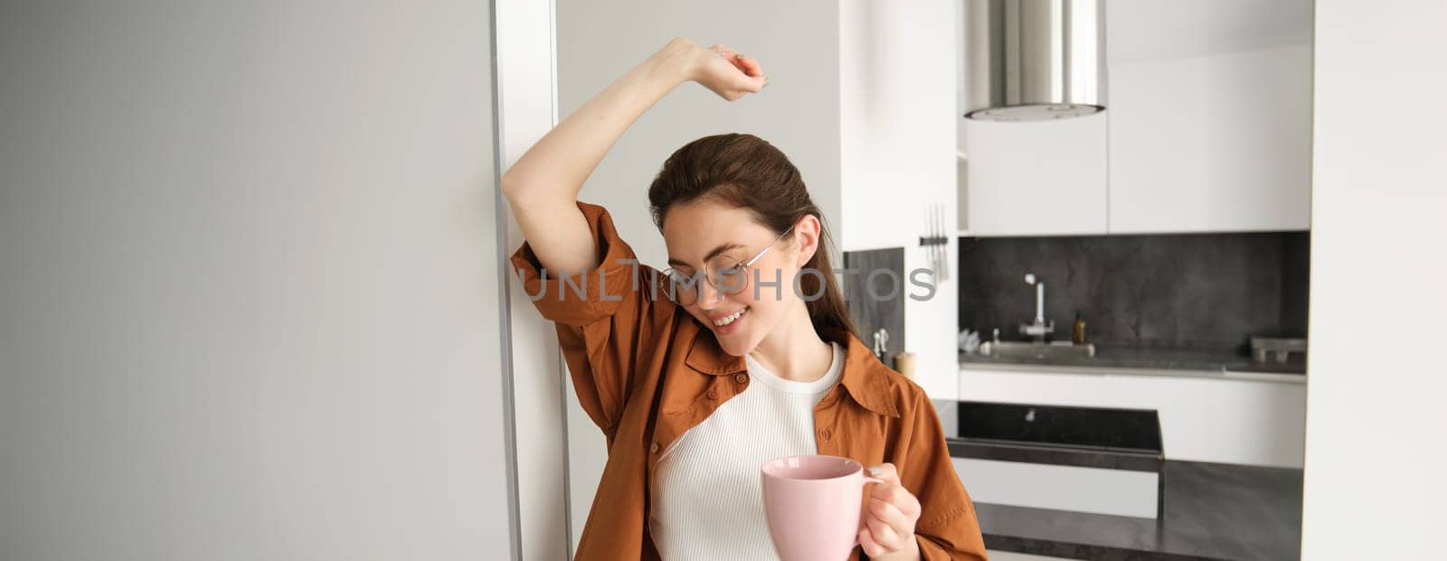 Portrait of carefree, beautiful young woman, relaxing at home, drinking cup of coffee.
