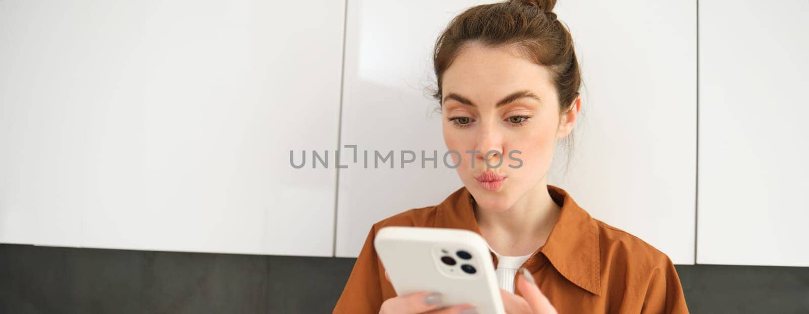 Portrait of young woman at home, looking with interest at smartphone screen, concept of online shopping, buying on mobile apps, picking something using application on phone by Benzoix