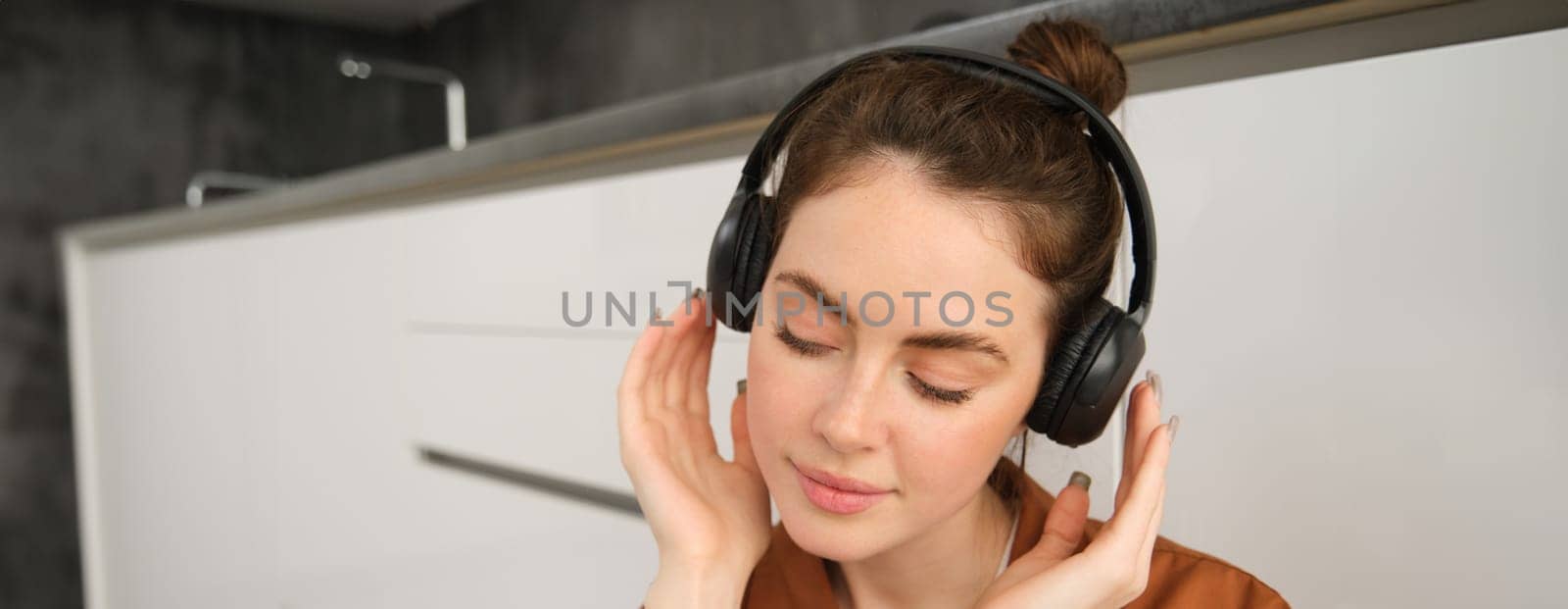 Close up shot of modern stylish woman in headphones, relaxes while listens to music in wireless earphones by Benzoix