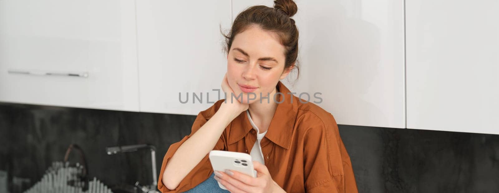 Portrait of beautiful young woman with smartphone, using mobile app, reading message or news feed on telephone by Benzoix