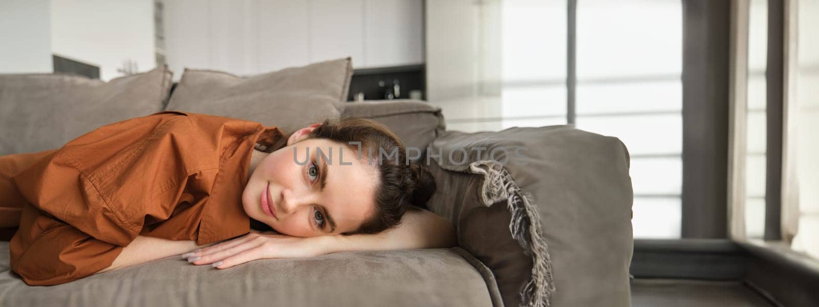 Portrait of beautiful smiling woman, resting at home, lying on couch, relaxing on weekend, looking at camera with happy face.