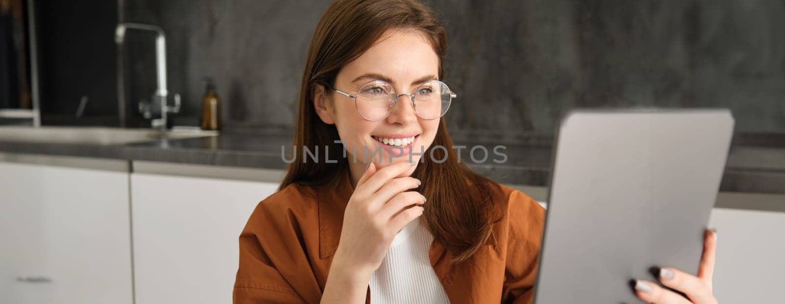 Portrait of young woman, student studying on remote, using digital tablet to study online course, e-learning, working from home in kitchen by Benzoix