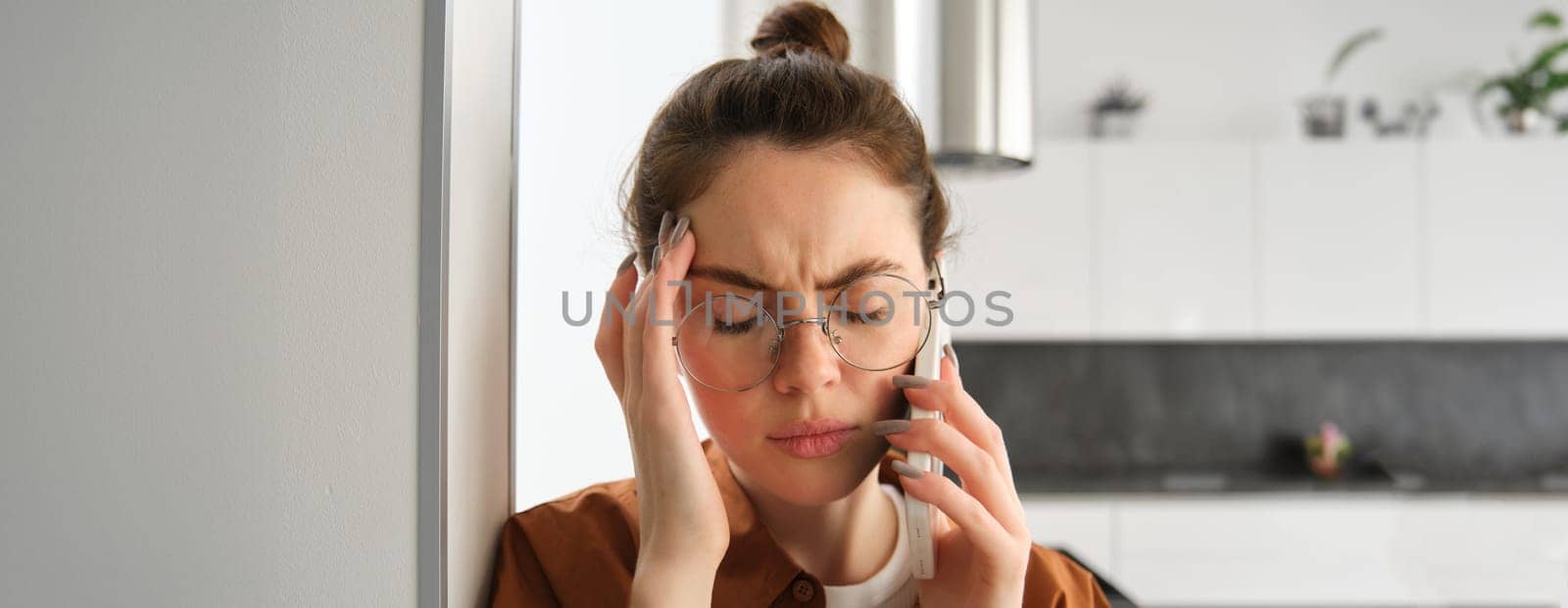 Close up portrait of young troubled, worried woman listens to voice message, having difficult phone conversation, answer a call and looking concerned, touching head by Benzoix