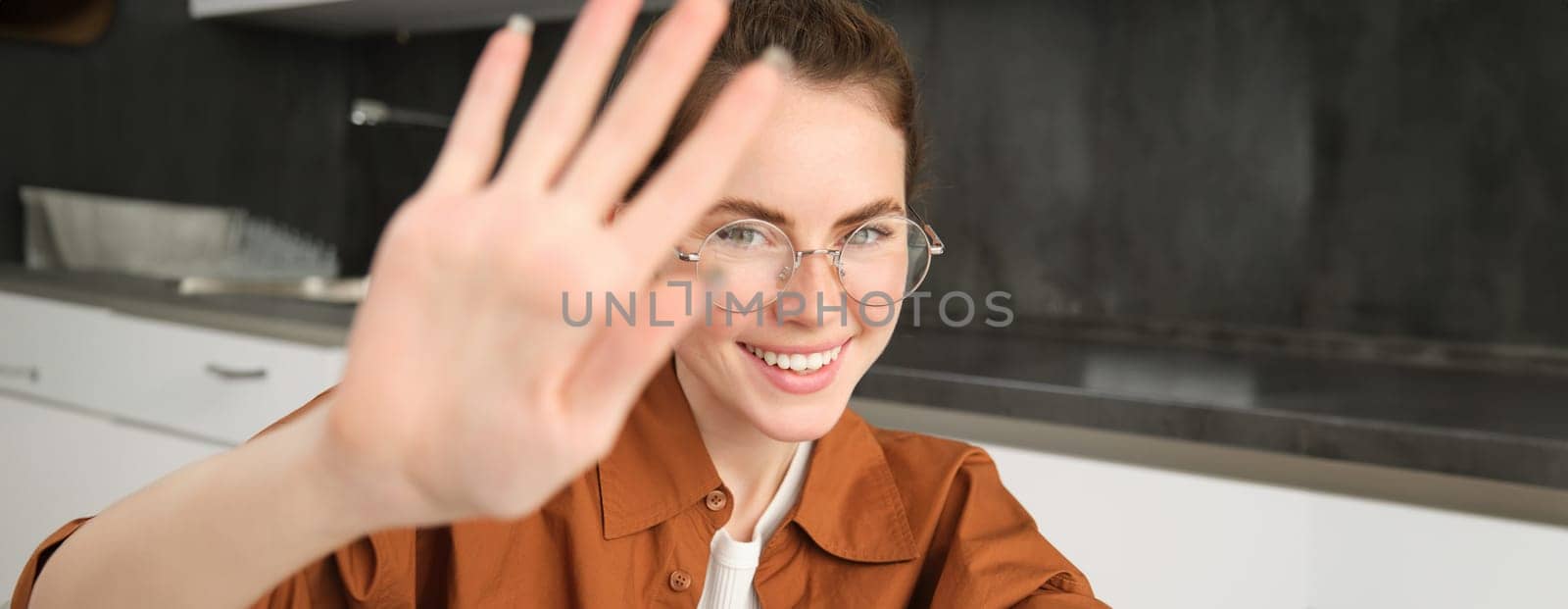 Portrait of cute girlfriend, blocks camera with extended hands, covers face and smiles, stop filming gesture, smiling and looking happy.