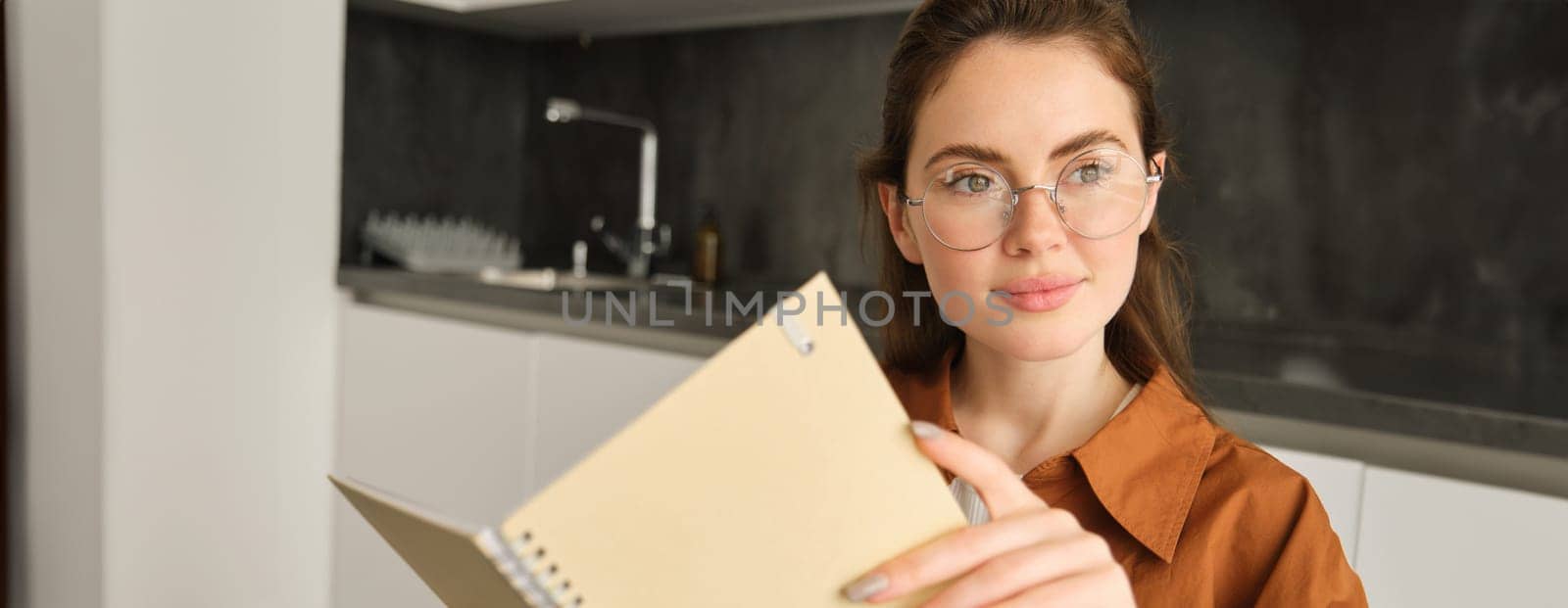 Portrait of beautiful young woman studying, student revising at home, doing homework, holding planner, reading her notes and smiling, writing in diary.
