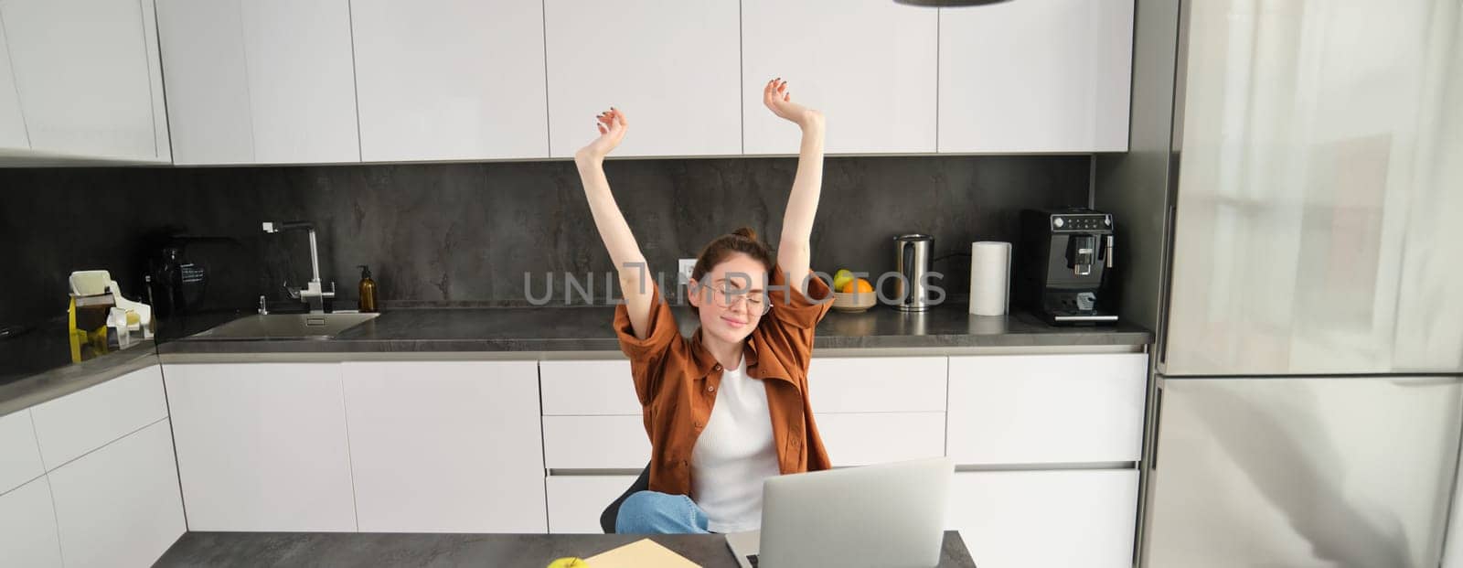 Portrait of cheerful young woman, student stretches her hands with pleased face, accomplish goal, finish working on project, using laptop and smiling pleased.