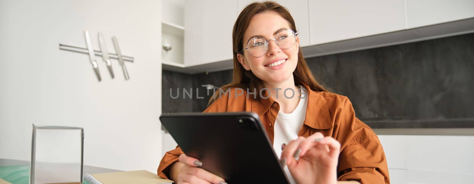 Portrait of young woman working from home, connecting to lesson on digital tablet, reading in glasses, studying remotely in her kitchen, distance learning and education concept by Benzoix