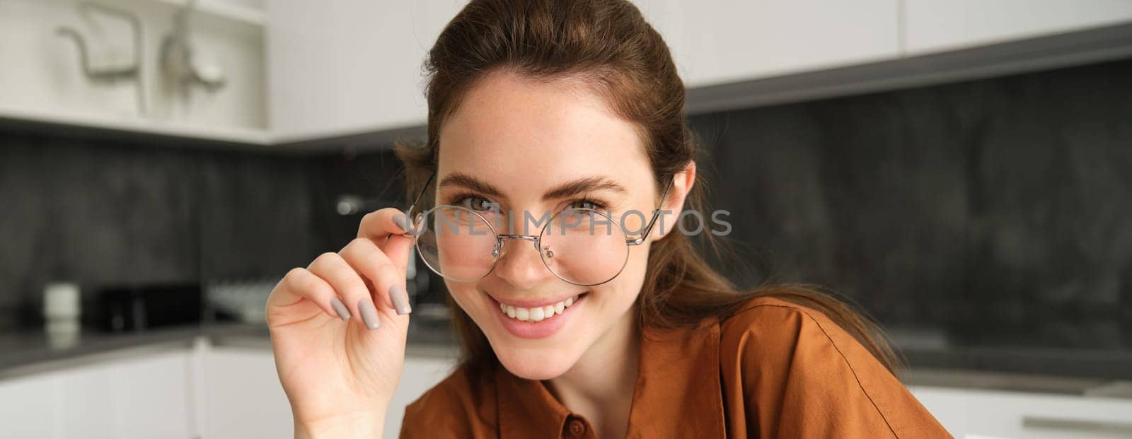 Close up portrait of happy, carefree young woman in her new glasses, showing her eyewear, laughing and smiling, posing in kitchen.