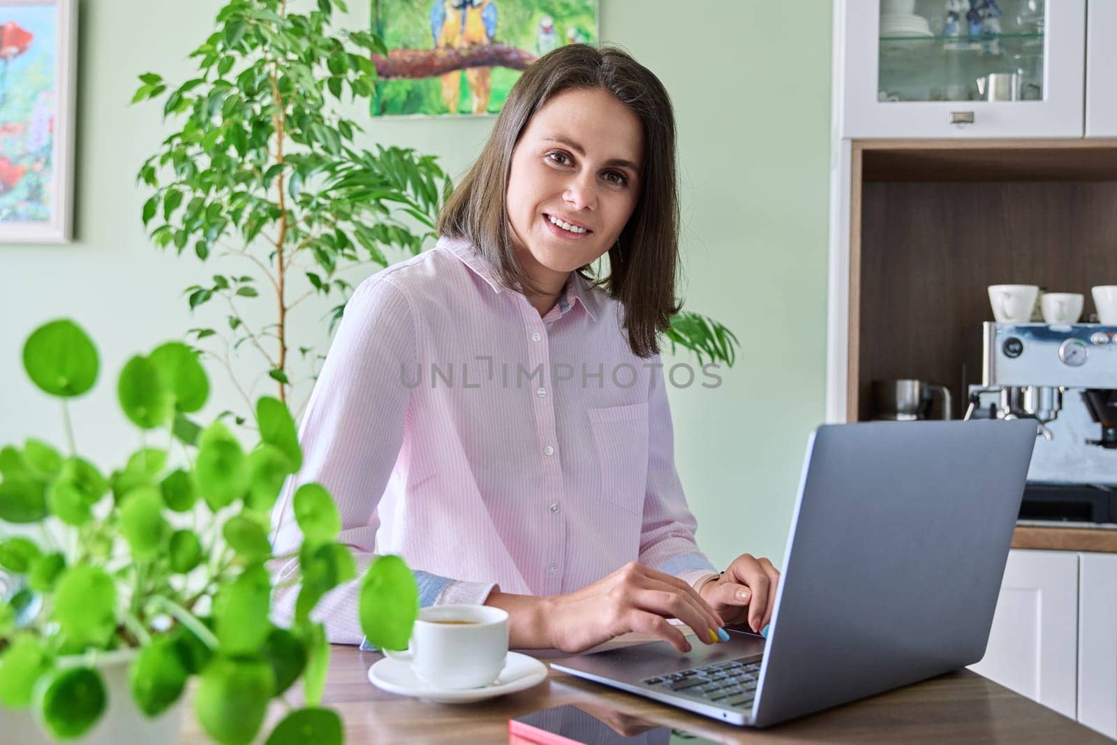 Smiling attractive young woman working at home using laptop, looking at camera. Lifestyle, freelancing, technology, job, work, leisure, people concept