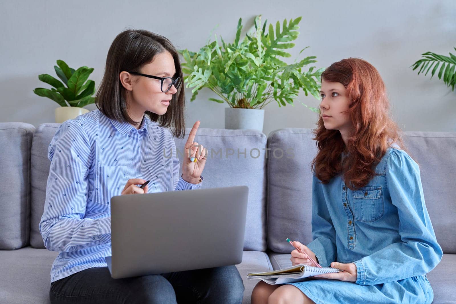 Preteen girl studying together with the teacher, in the office on the couch