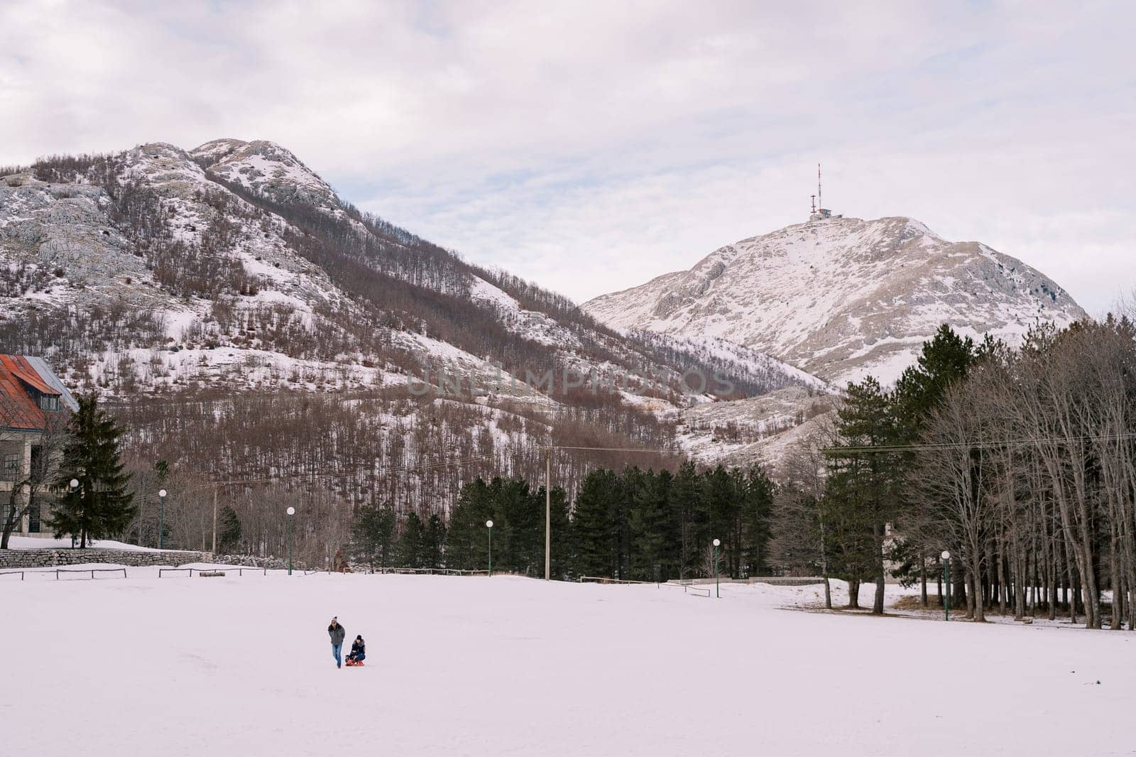 Man carries a woman on a sled across a snow-covered plain at the foot of the mountains. High quality photo