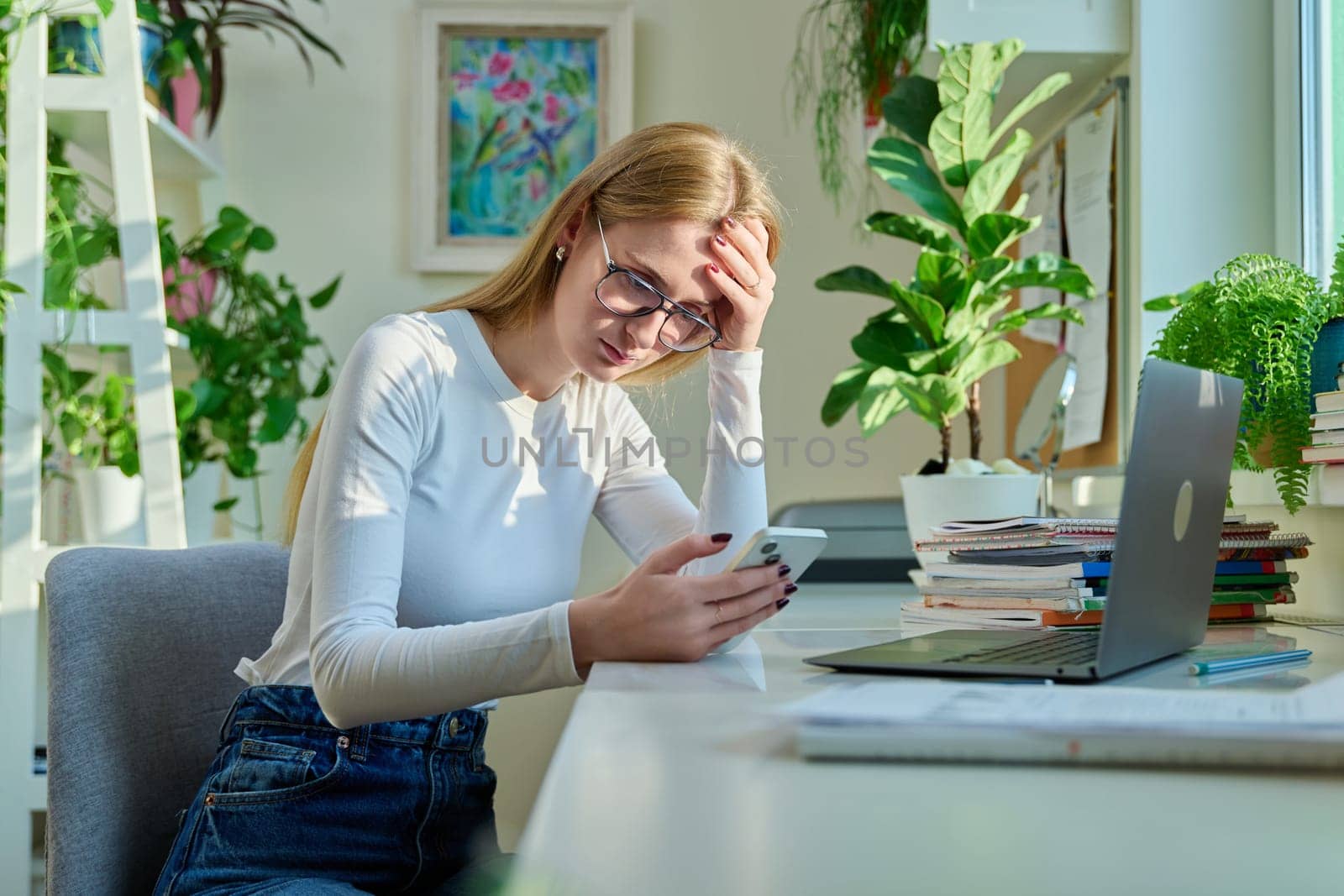 Serious sad teenage female sitting at home reading texting on smartphone. Social life, communication, study education, lifestyle technology concept