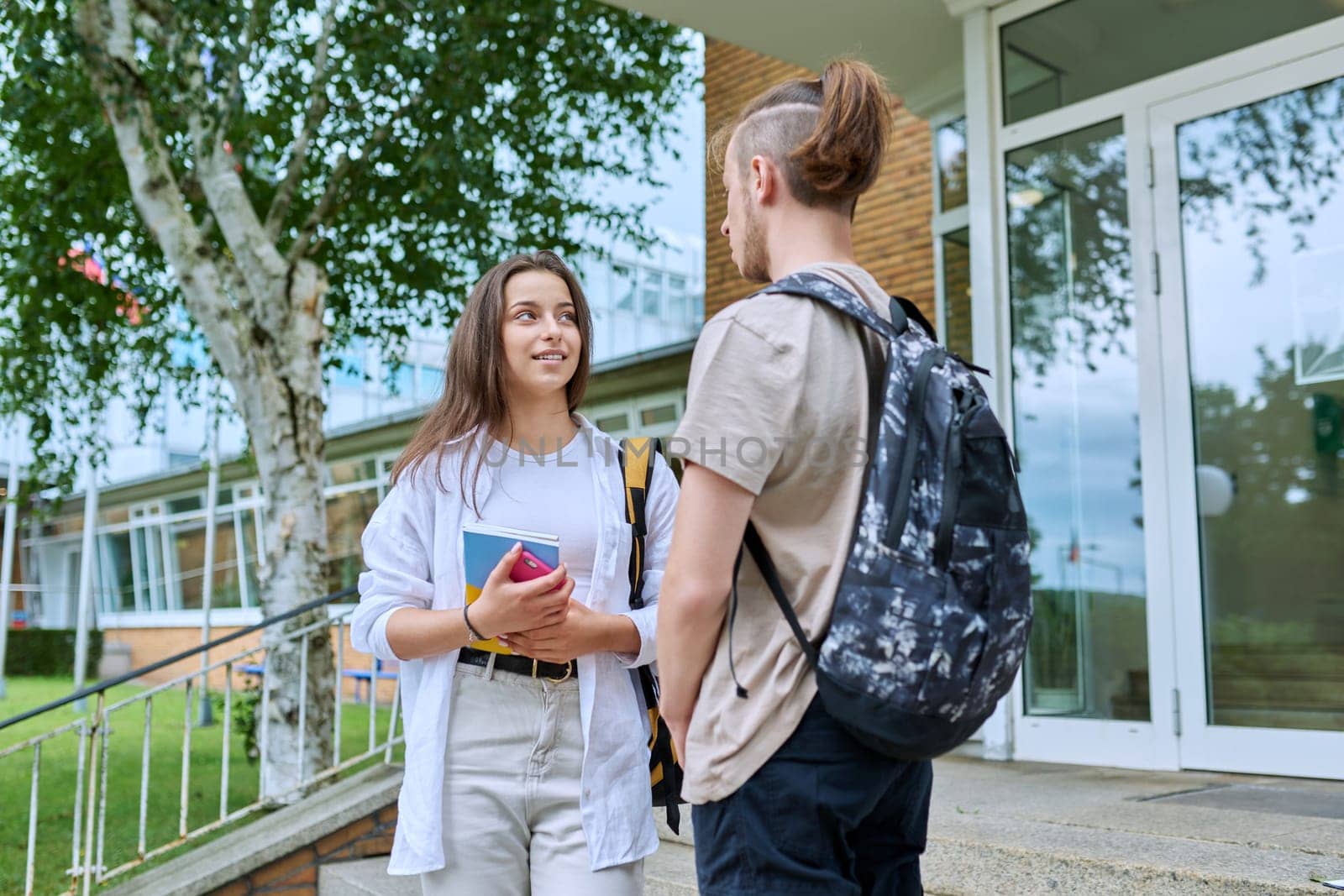 Meeting of two teenage students, guy and girl, outdoors near educational building. Friendship, communication, education, high school college concept