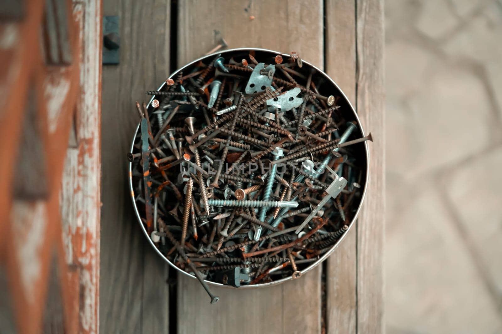 Old vintage nails in a round box lie on the porch of a wooden country house, top view. Old things for workshop and recycling and creative work.
