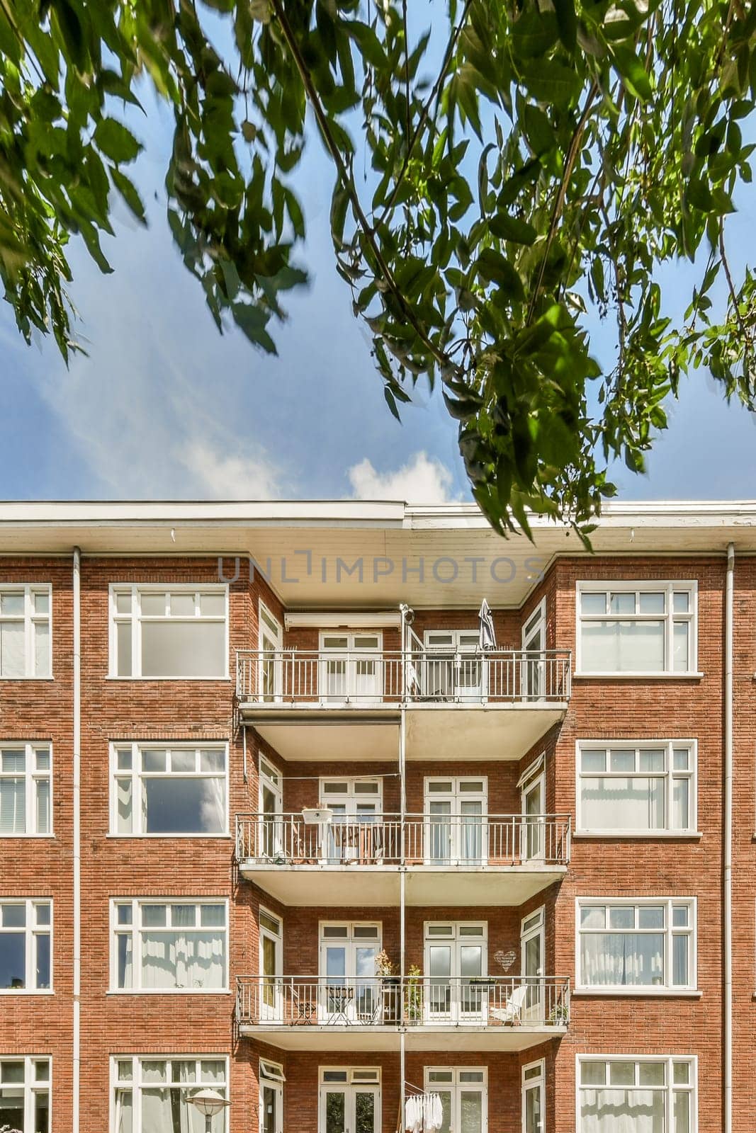 a brick apartment building with balks on the balcony and green trees in the fore - swayr stock photo