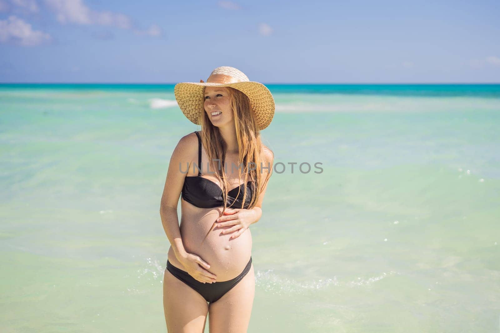 Radiant and expecting, a pregnant woman stands on a pristine snow-white tropical beach, celebrating the miracle of life against a backdrop of natural beauty.