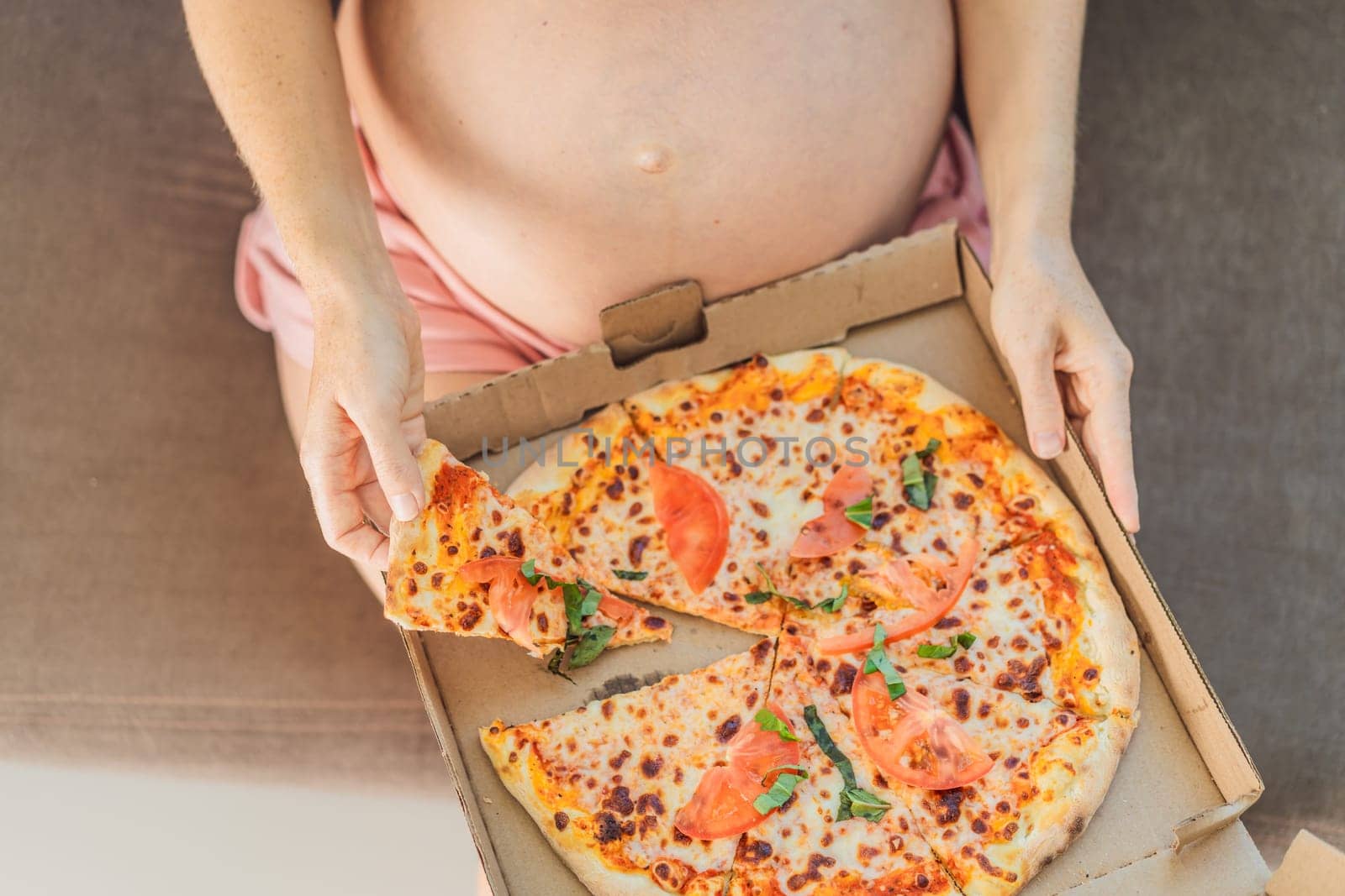 A pregnant woman enjoys a slice of pizza, savoring a moment of indulgence while satisfying her craving for a delightful, comforting treat. Excited Pregnant Young Lady Enjoying Pizza Holding Biting Tasty Slice Posing With Carton Box. Junk Food Lover Eating Italian Pizza. Unhealthy Nutrition Cheat Meal.