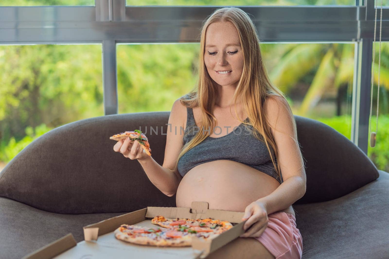 A pregnant woman enjoys a slice of pizza, savoring a moment of indulgence while satisfying her craving for a delightful, comforting treat. Excited Pregnant Young Lady Enjoying Pizza Holding Biting Tasty Slice Posing With Carton Box. Junk Food Lover Eating Italian Pizza. Unhealthy Nutrition Cheat Meal by galitskaya