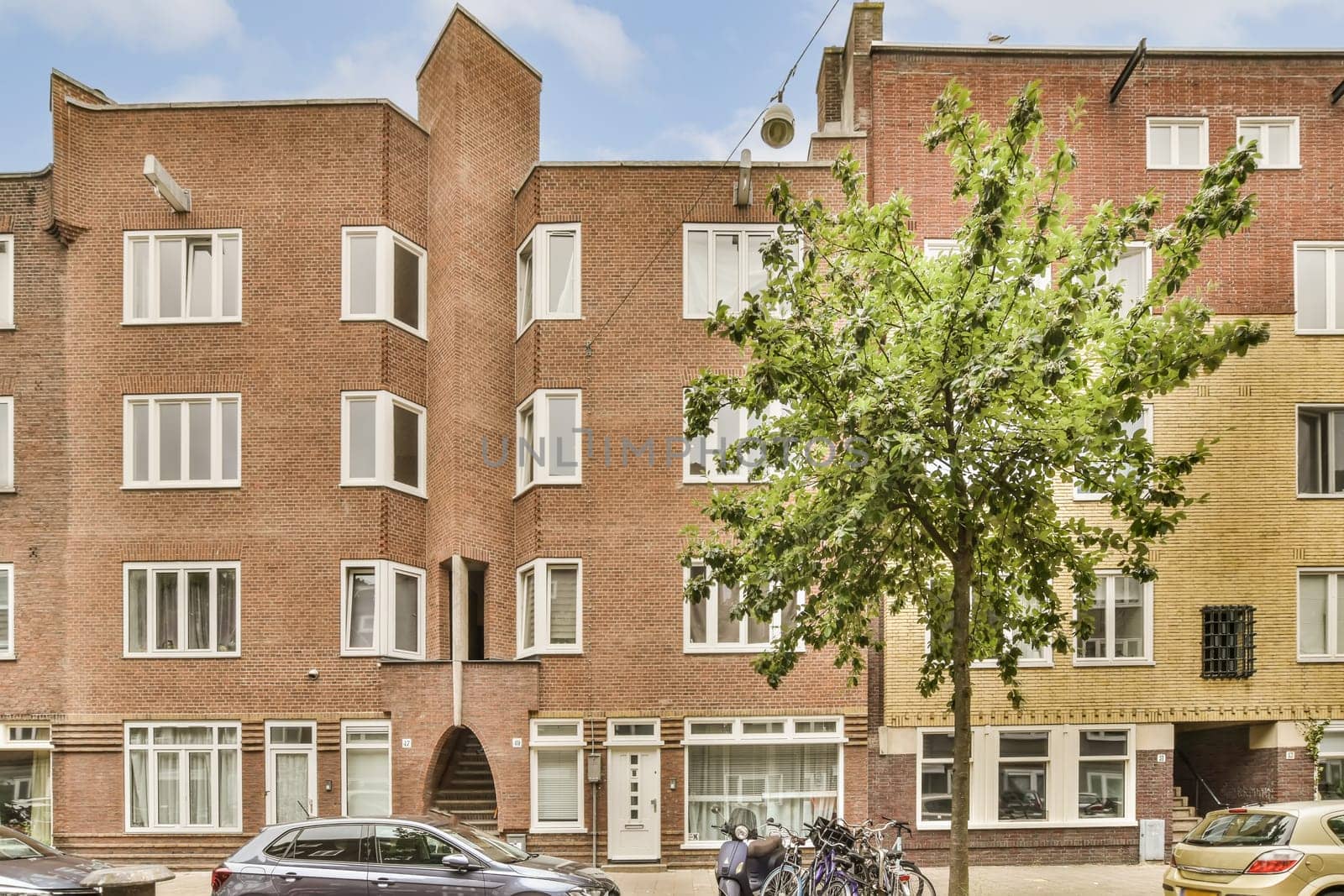 an apartment building with cars parked in the street next to it and a tree growing on the side of the road